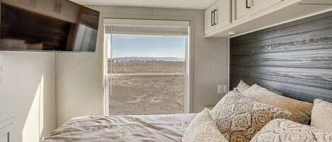 A bedroom with a bed, pillows, a window, and a view of the outdoors.
