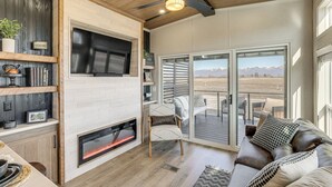 Ett modernt vardagsrum med en öppen spis, en soffa, en tv och en skjutdörr i glas som leder ut till en terrass.