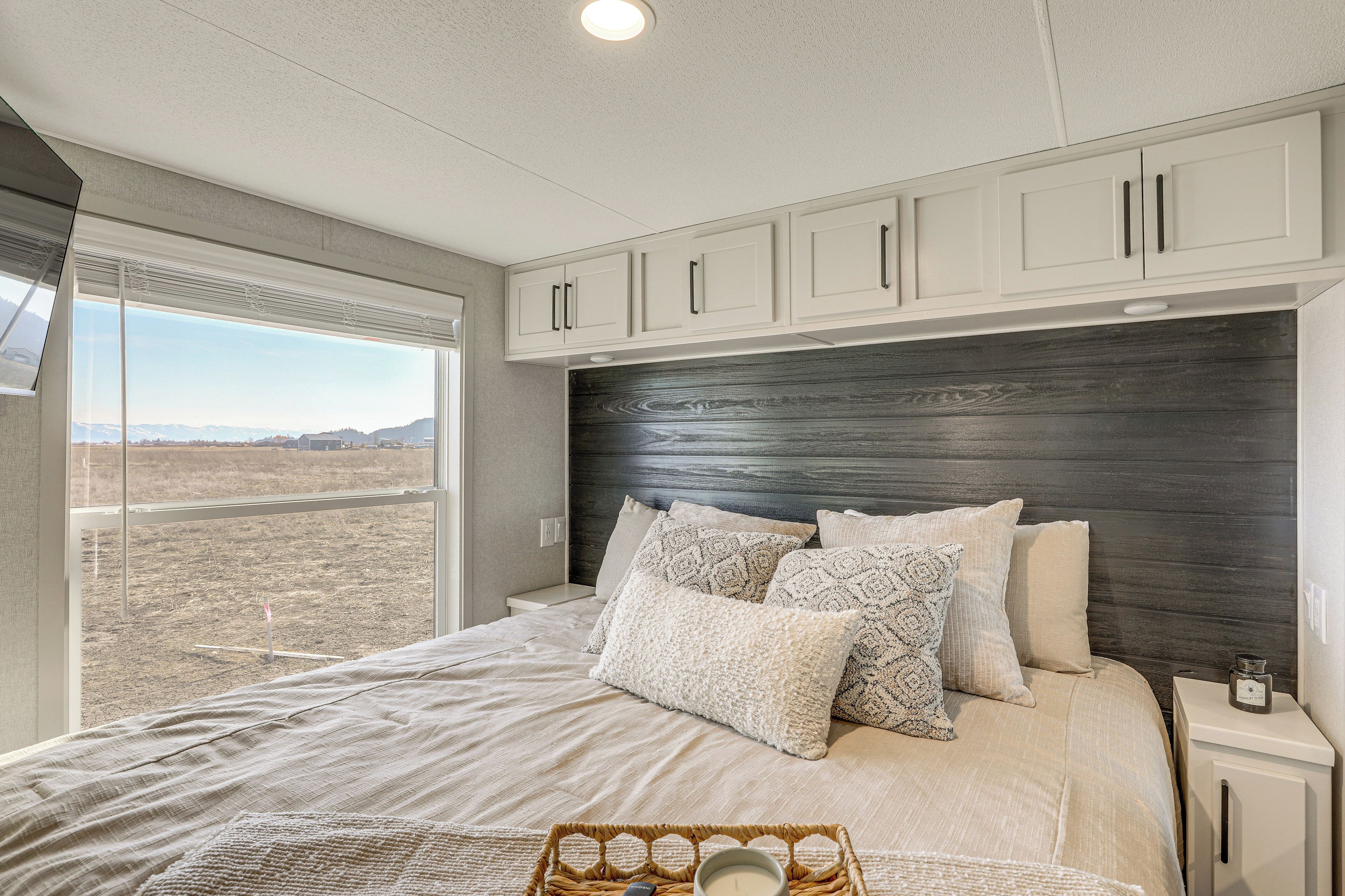 Ein Schlafzimmer mit einem großen Bett, einem Kopfteil, einem Nachttisch, einem Fenster und Blick auf die Landschaft.
