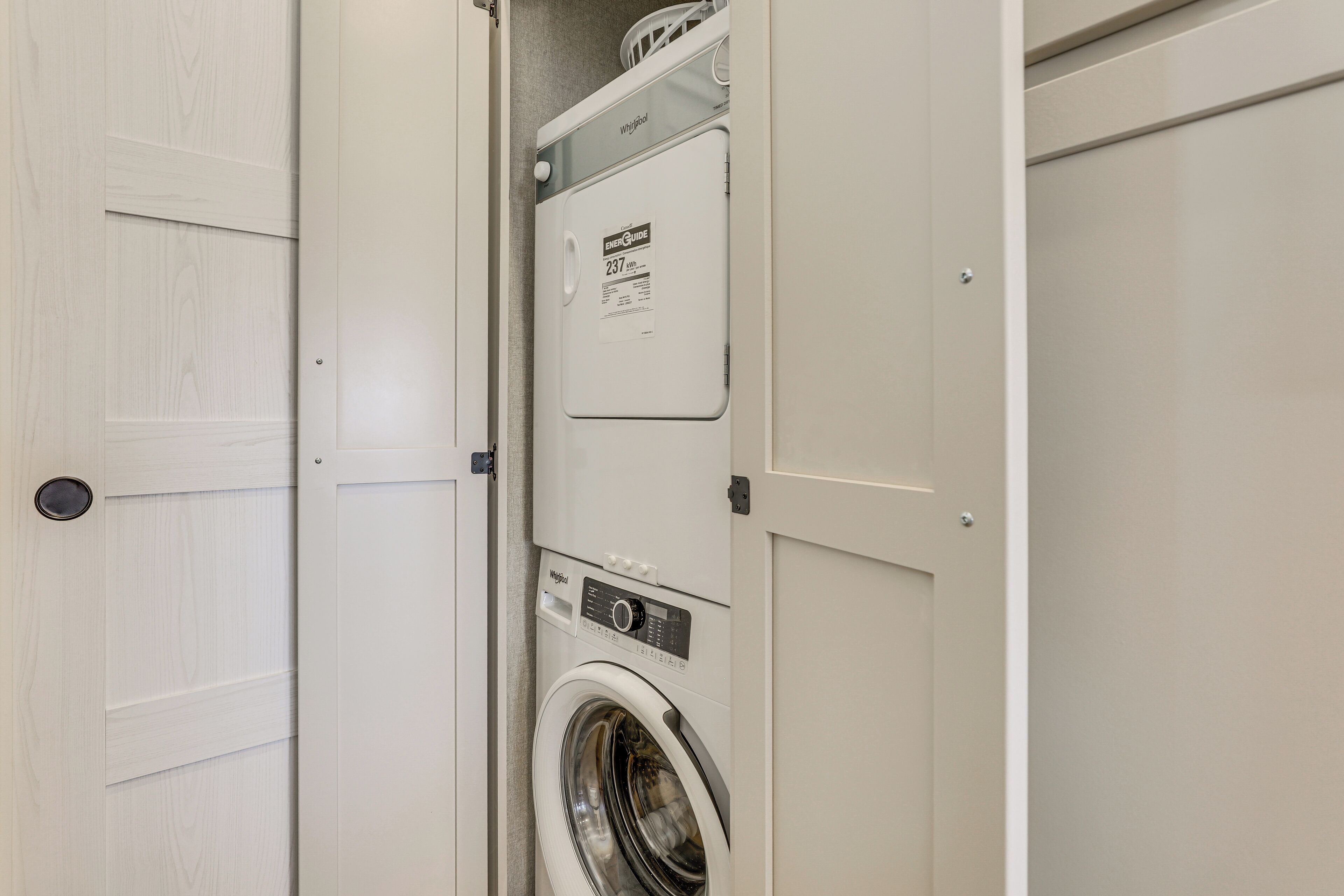 A compact laundry room with a front-loading washer and dryer, a white door, and a small window above the dryer.