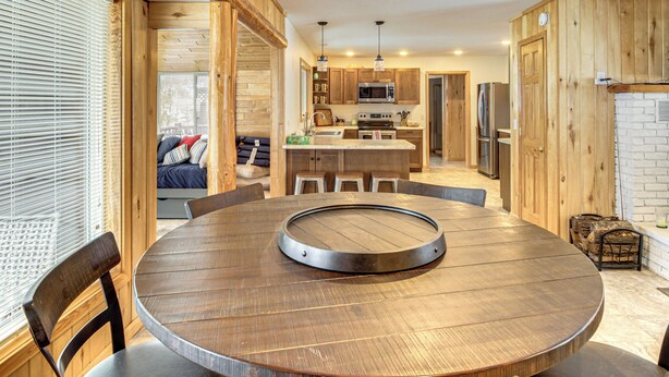 A circular wooden dining table with chairs, a kitchen with wooden cabinets, a microwave, and a refrigerator. - Waterfront Leech Lake Cabin w/ Boat Dock + Lift (Walker)
