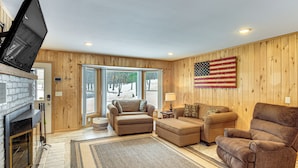 A living room with a fireplace, a large American flag, and a view through the glass doors. - Waterfront Leech Lake Cabin w/ Boat Dock + Lift (Walker)