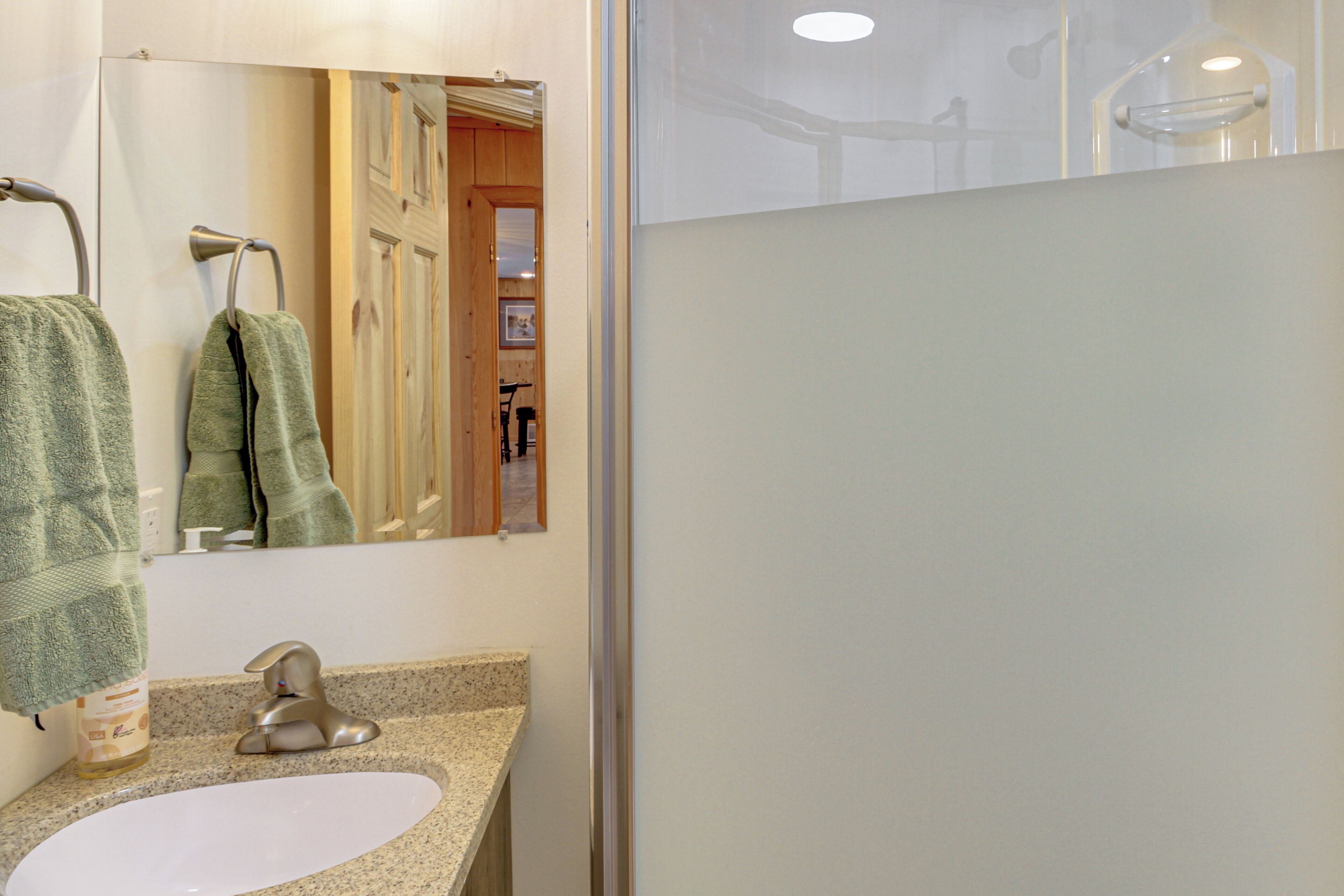 A bathroom with a sink, mirror, towel rack, and shower area.
