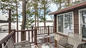 A covered outdoor area with wicker chairs, a wooden deck, and a view of trees and snow. - Waterfront Leech Lake Cabin w/ Boat Dock + Lift (Walker)