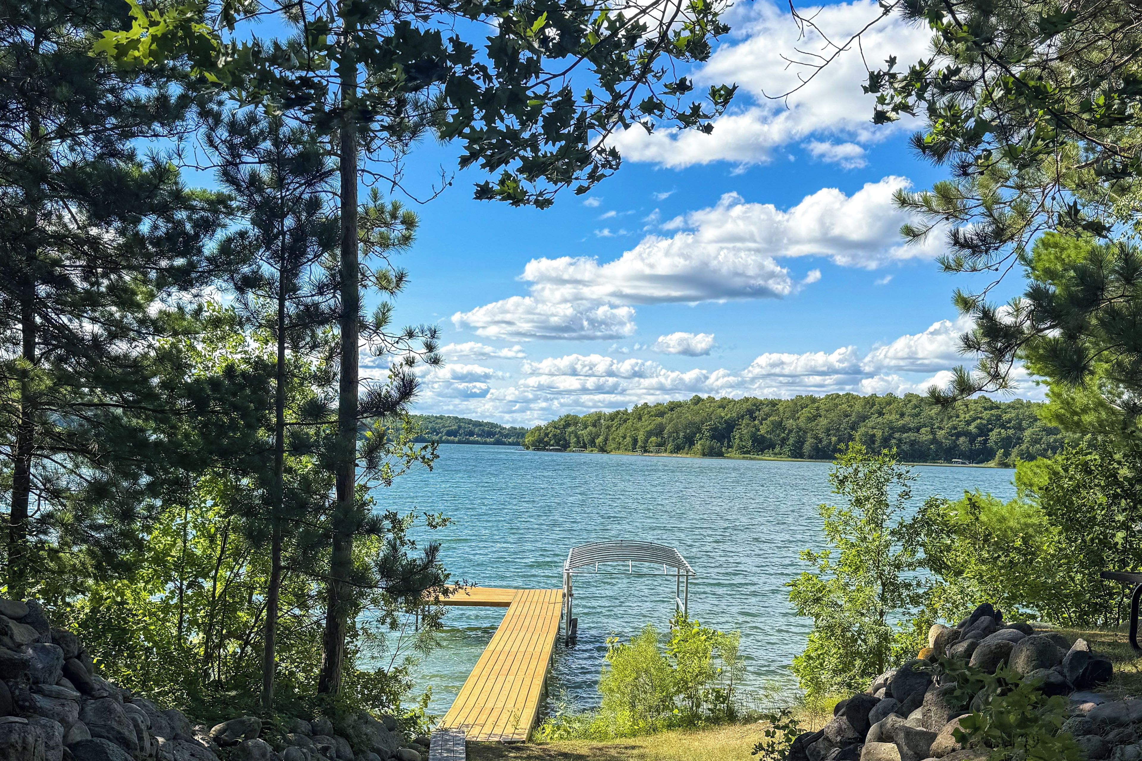 A wooden dock extending into a lake surrounded by trees and a clear sky.