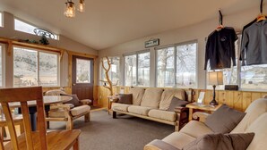 A cozy room with a wooden floor, a sofa, a chair, a table, and a window with a view of a hill. - Mtn-view Ranch Retreat in Western Wyoming! (Thermopolis)