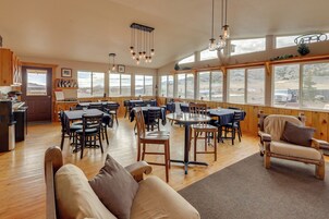 Un comedor amplio con mesas y sillas de madera, ventanas grandes con vistas y lámparas colgantes.