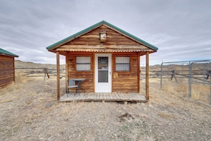 A wooden cabin with a front porch, a table, and a chair.