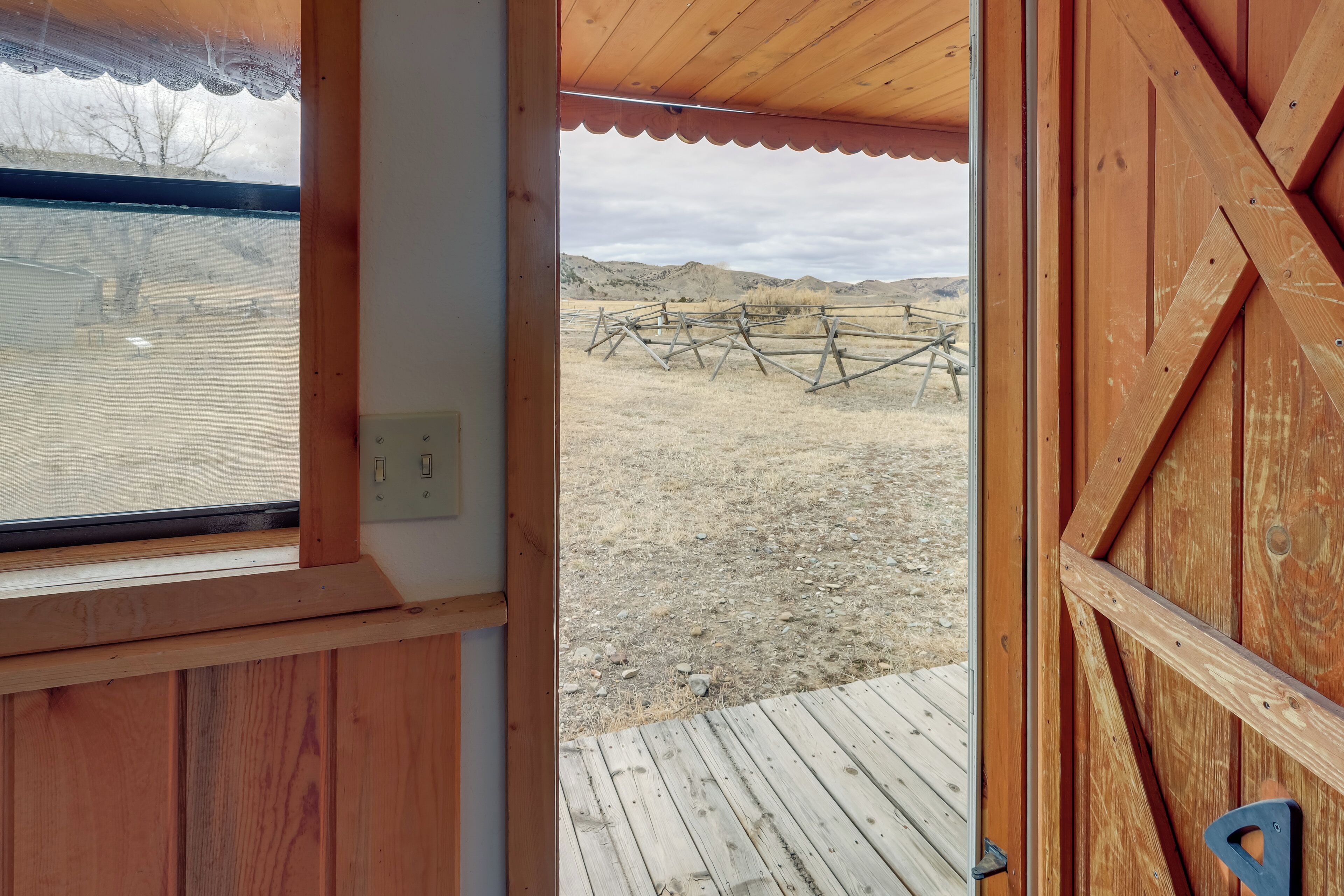 A wooden door leading to an outdoor area with a wooden deck and a view of a fenced field.