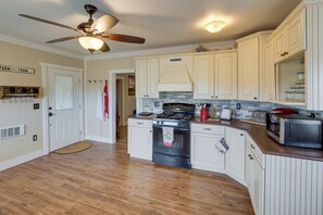 A kitchen with white cabinets, a stove, a microwave, and a ceiling fan.