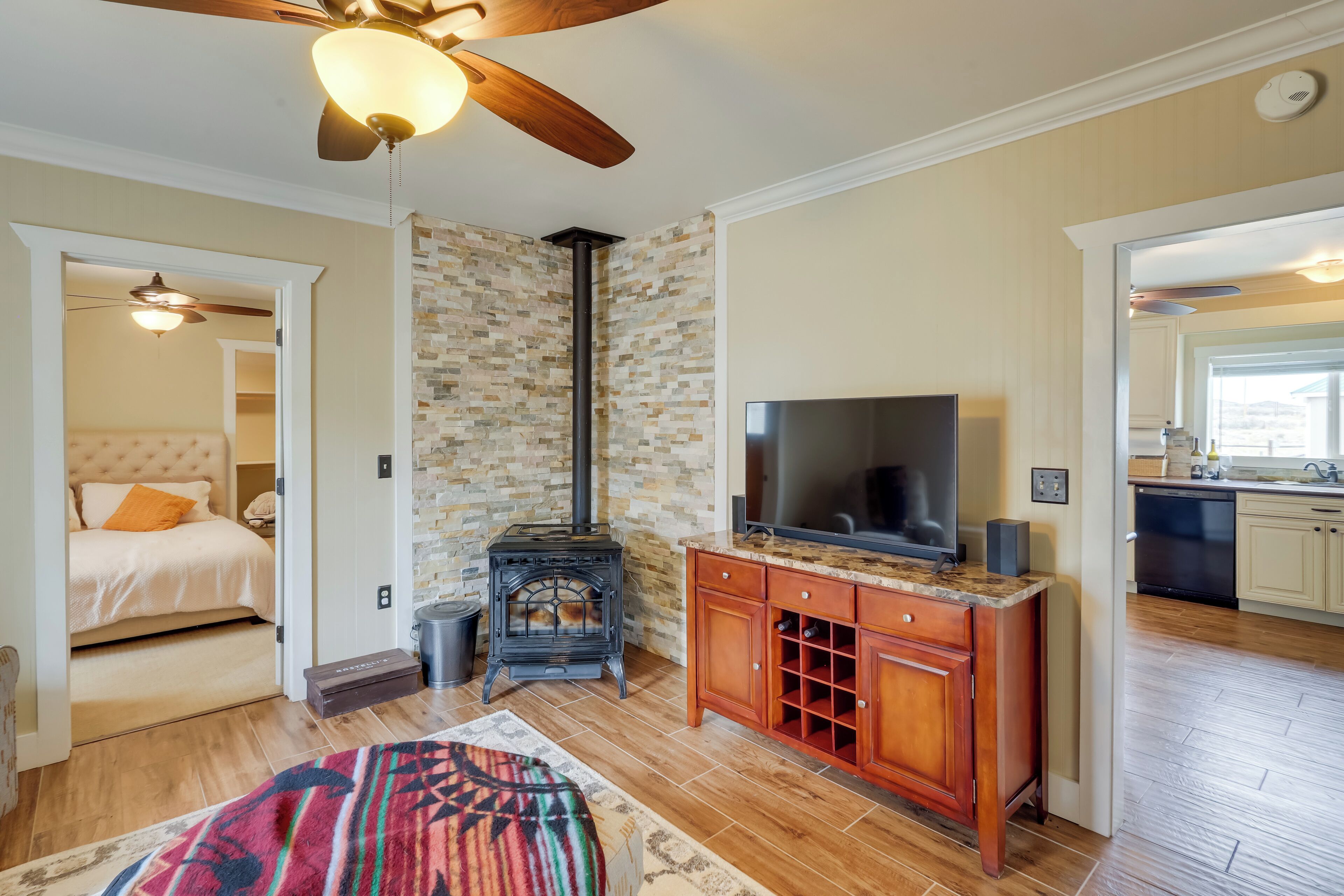 A cozy living room with a fireplace, a television, and a kitchen area visible through an open door.