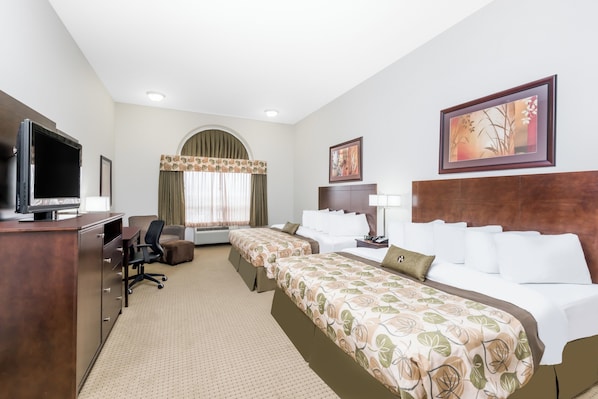Quarto de hotel com televisão, secretária, duas camas, uma cadeira, luminária de mesa, quadro emoldurado e janela com cortinas.
