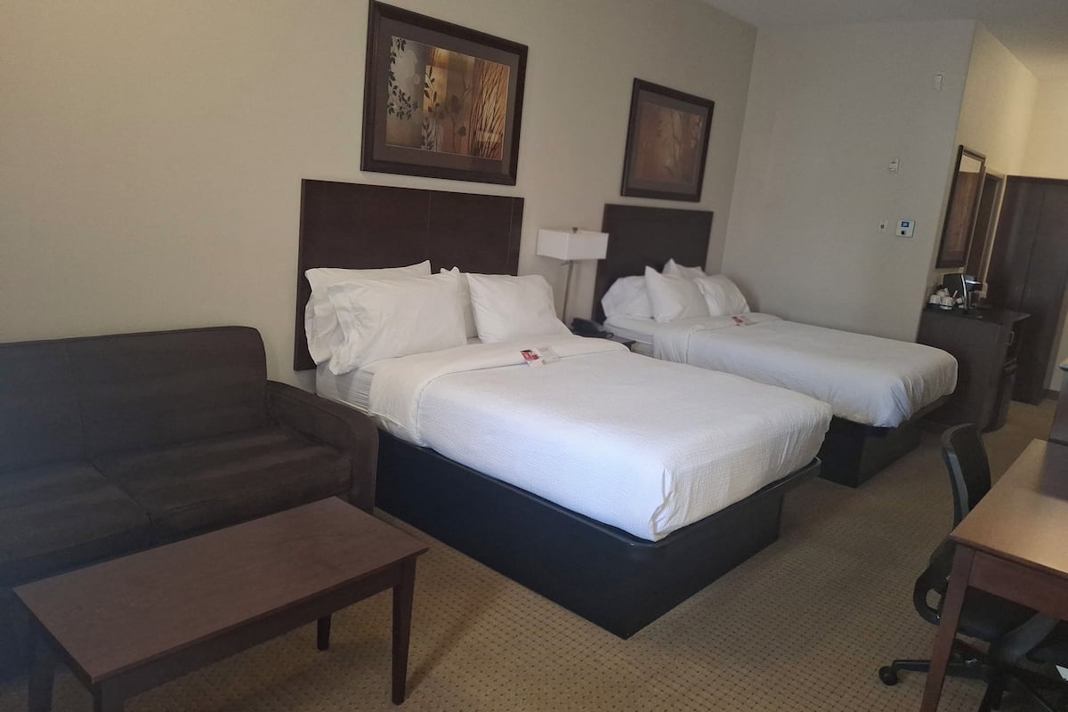 A hotel room with two beds, a sofa, a small table, and a desk.