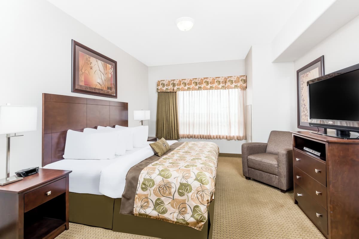 A hotel room with a bed, a TV, a chair, a desk, and a window with curtains.