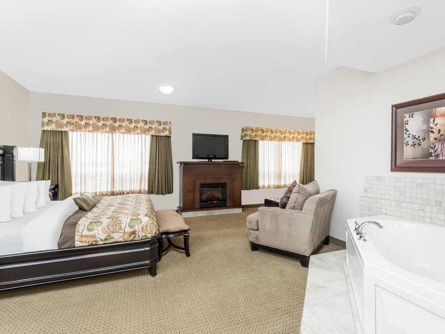 A hotel room with a bed, a sofa, a chair, a fireplace, a television, and a bathtub.