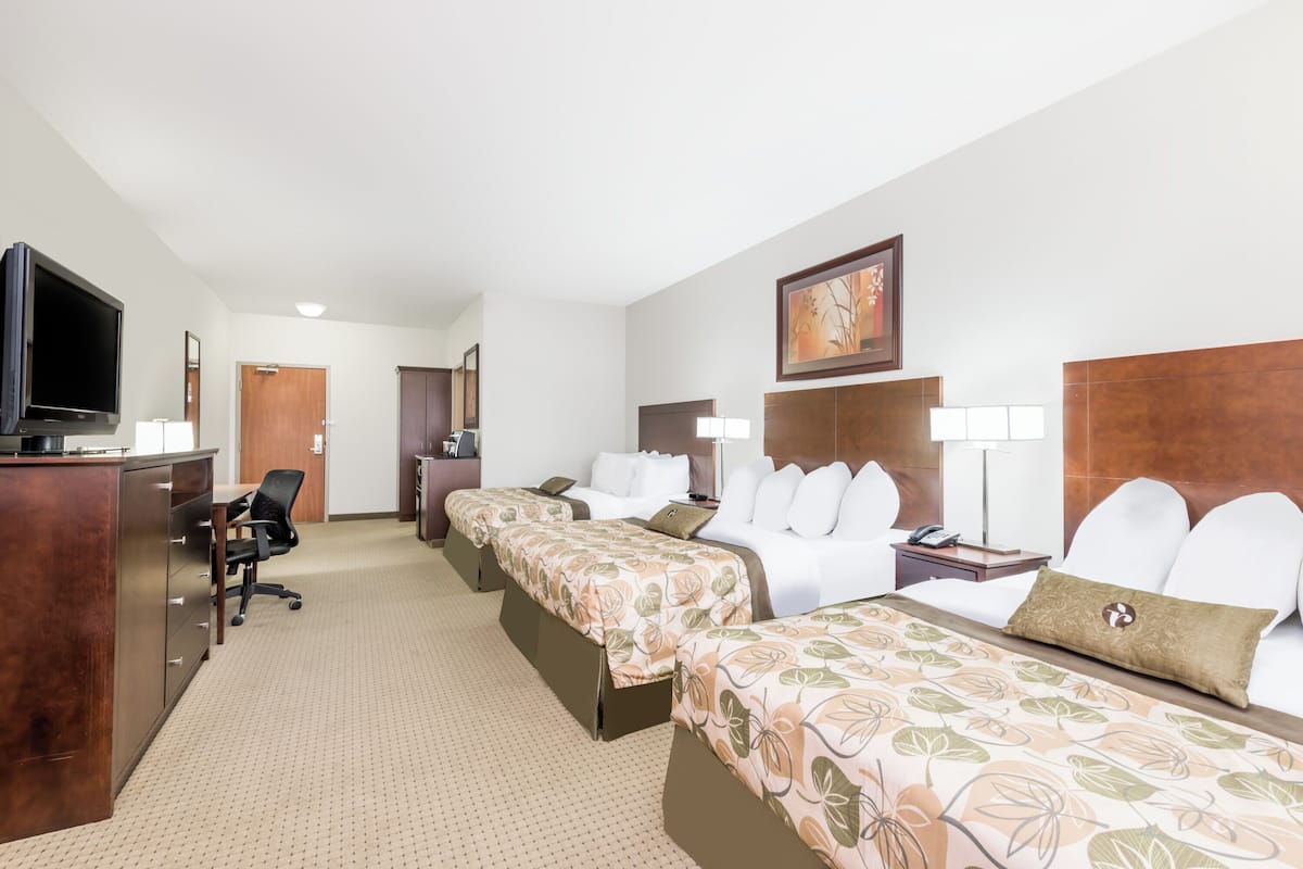 A hotel room with two beds, a desk with a TV, a chair, and a door.
