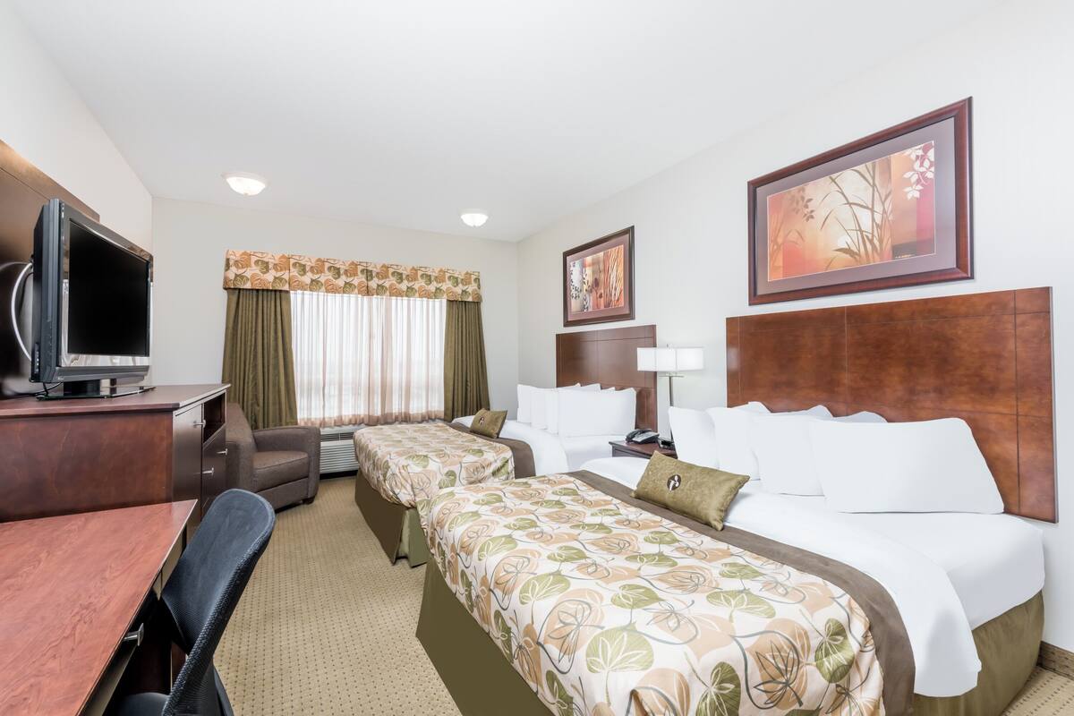A hotel room with two beds, a desk, a TV, and a painting on the wall.
