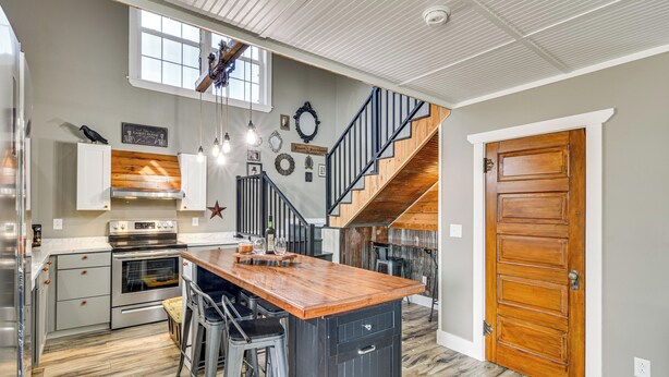 A kitchen with a central island, bar stools, a staircase, and a wooden door.
