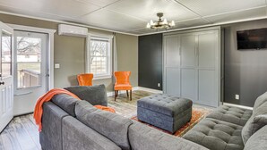 A living room with a sectional sofa, an ottoman, a chair, a chandelier, and a TV mounted on the wall.