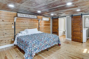 A bedroom with a wooden headboard, a bed with a floral bedspread, a wall-mounted air conditioner, and a sliding door leading to a bathroom. - Shenandoah Valley Retreat: Hike, Fish & Explore! (Broadway)