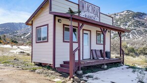 Un piccolo edificio con un cartello che riporta la scritta 'OMIAKINBAH RANCH' in un ambiente rurale, con montagne sullo sfondo.