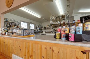 Una zona de bar con mostrador de madera, estantes con botellas y una ventana al fondo.