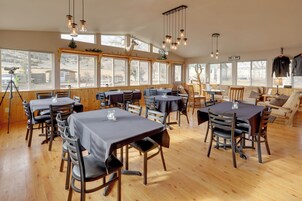 Un comedor amplio con varias mesas y sillas, ventanas grandes y un interior de madera.