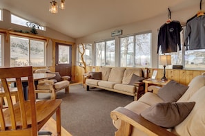 A cozy room with a wooden floor, a sofa, a chair, a table, and a window with a view of a hill. - On Ranch w/ Stunning Mtn Views! Thermopolis Escape (Thermopolis)