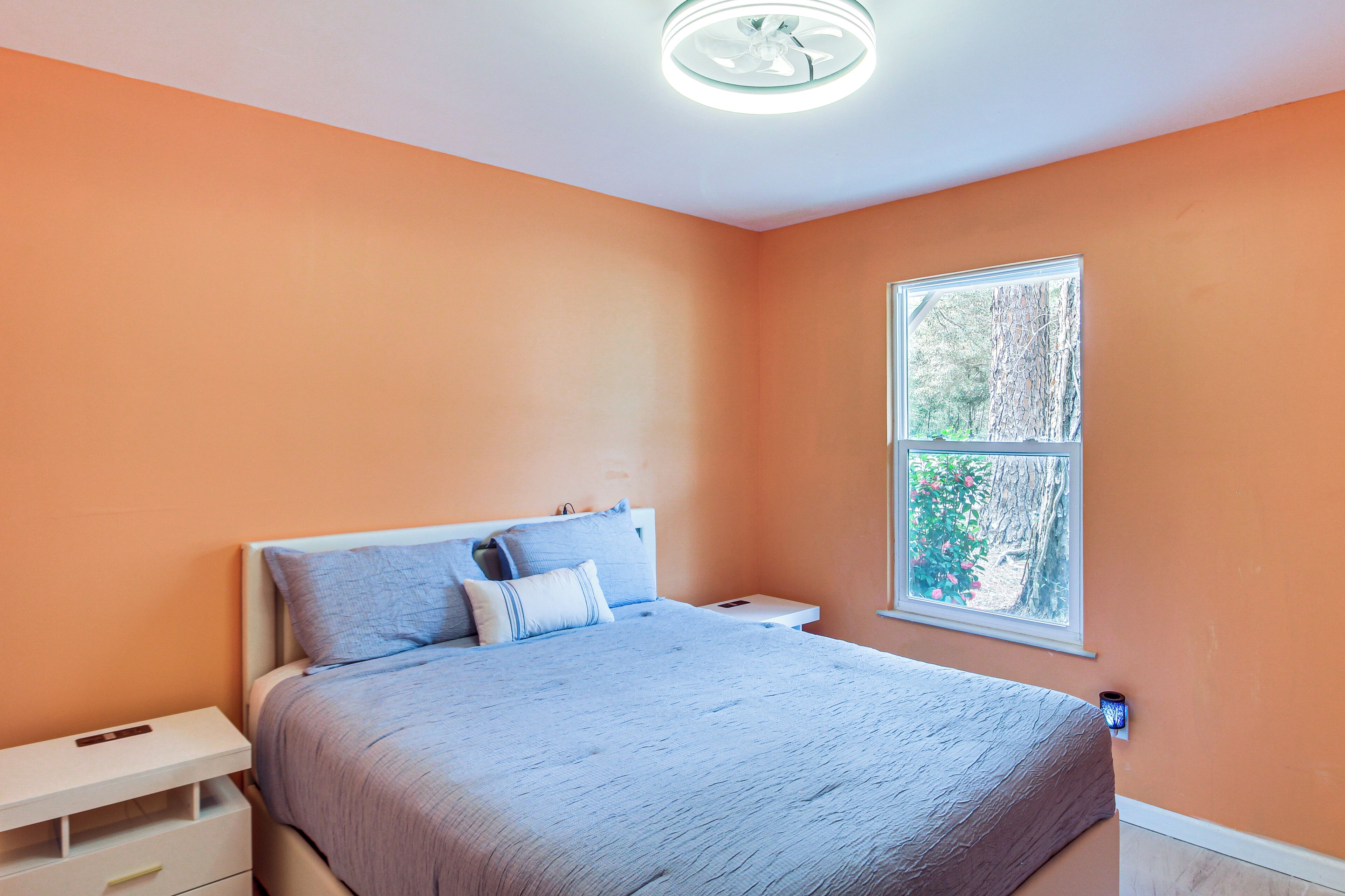 A bedroom with a bed, nightstand, and a window with a view of trees.