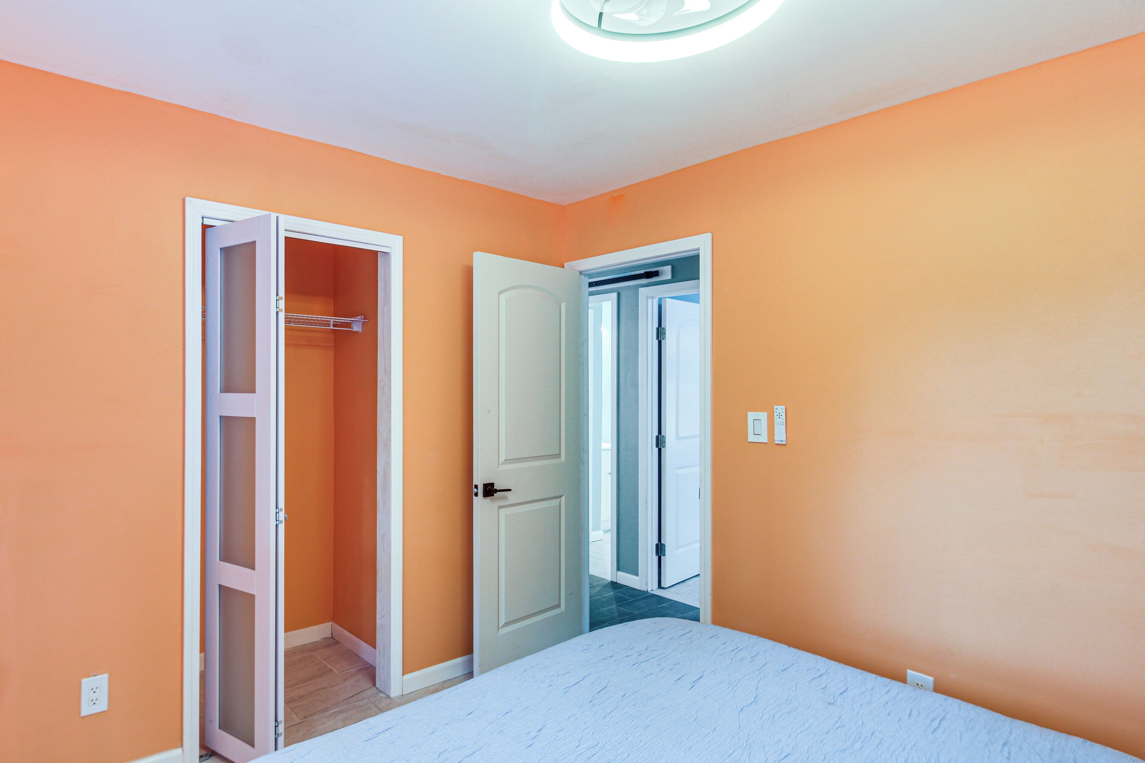 Quarto com closet aberto, porta para outro cômodo e uma cama.