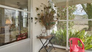 Un porche cubierto con una mesa, una silla y un jarrón con plumas de pavo real secas.