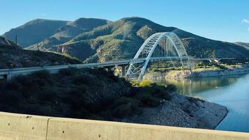 A bridge with a steel arch design over a river, surrounded by hills and vegetation.