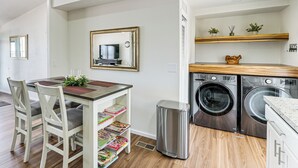 A compact kitchen with a dining table, chairs, a trash bin, and a washing machine.