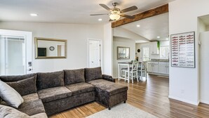 A living room with a sectional sofa, a ceiling fan, and a kitchen in the background.