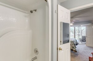Un baño con bañera, ducha y una puerta que da a un dormitorio con cama y sillón.