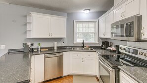 A kitchen with white cabinets, a dishwasher, a stove, and a microwave. - Private Dock + River View: Cabin Retreat in Jesup (Jesup)