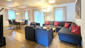 A spacious living room with a sofa set, a dining area with chairs, and a television. - 5_3 Chalet Noriker by Interhome (Niedernsill)