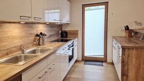 A modern kitchen with wooden countertops, stainless steel appliances, and a sliding glass door leading to a balcony. - 5_3 Chalet Noriker by Interhome (Niedernsill)