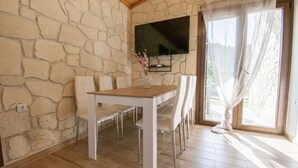Zona pranzo con parete in pietra, televisione a schermo piatto sopra un tavolo e finestra con tende leggere.