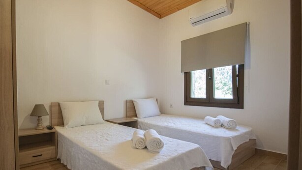 Una camera da letto con due letti, un comodino, una lampada, una finestra con tenda e un climatizzatore.