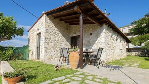 Un edificio in pietra con tetto in tegole, un patio con sedie e una pianta in vaso.