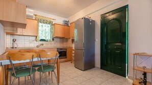 A kitchen with a dining table, chairs, a refrigerator, and a green door. - Aegean Maisonette by RentalsPro - Kryopigi (Kriopighi)