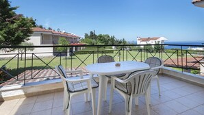 A balcony with a table and chairs, a view of the sea, and a fenced garden area. - Aegean Maisonette by RentalsPro - Kryopigi (Kriopighi)