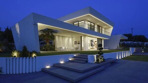 A modern two-story house with a flat roof, large windows, and a well-lit outdoor area with steps leading to the entrance. - Μaraviglia Ethereon Villa by RentalsPro (Nikiti)