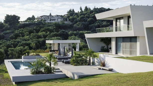 A modern house with a swimming pool, outdoor seating, and a view of a forested hill. - Μaraviglia Ethereon Villa by RentalsPro (Nikiti)