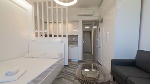 Ein Hotelzimmer mit einem Bett, einer Couch, einem kleinen Tisch, einem Korbstuhl und einer Küchenzeile im Hintergrund.