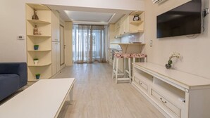 Eine moderne Küche mit Flachbildfernseher, eine Essecke mit Tisch und Stühlen sowie ein Wohnbereich mit einer Couch.