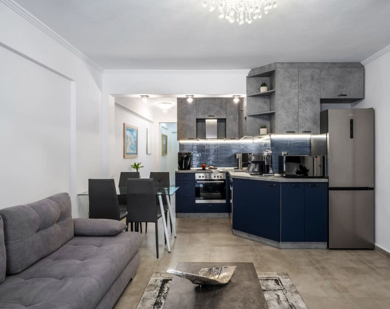 A modern kitchen with built-in appliances, a dining area with a gray sofa and chairs, and a small island.