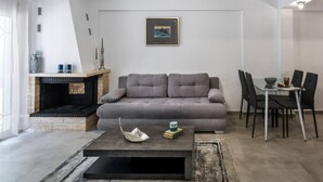 A living room with a sofa, a coffee table, a fireplace, and a dining area with chairs. - GnG Apartment 1 by RentalsPro - Nea Flogita (Nea Flogita)