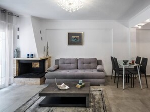 A living room with a sofa, a coffee table, a fireplace, and a dining area with chairs. - GnG Apartment 1 by RentalsPro - Nea Flogita (Nea Flogita)
